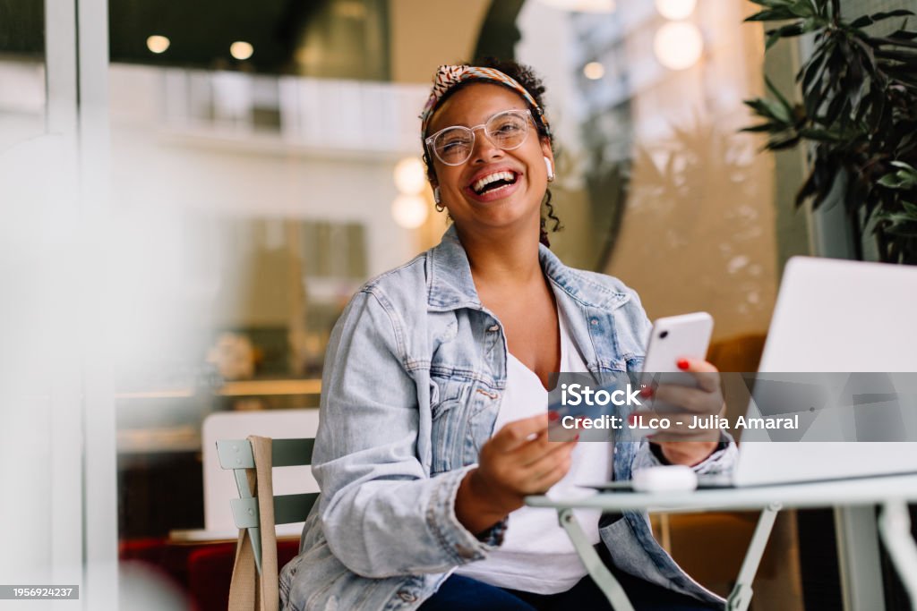 Young woman in a café happily uses her smartphone for online shopping and mobile banking, paying with a credit card. Woman highlighting the convenience of wireless technology and internet banking for digital transactions.