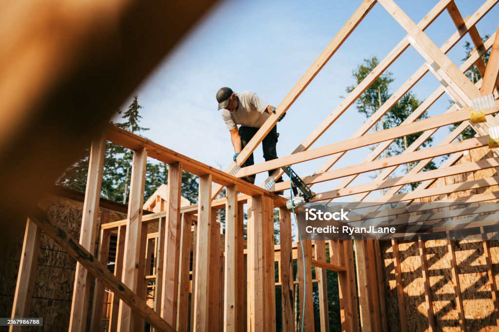 Workers build the frame of a new house project. Bare plywood and beams as it is framed up from the foundation. High lumber costs have affected the building process.