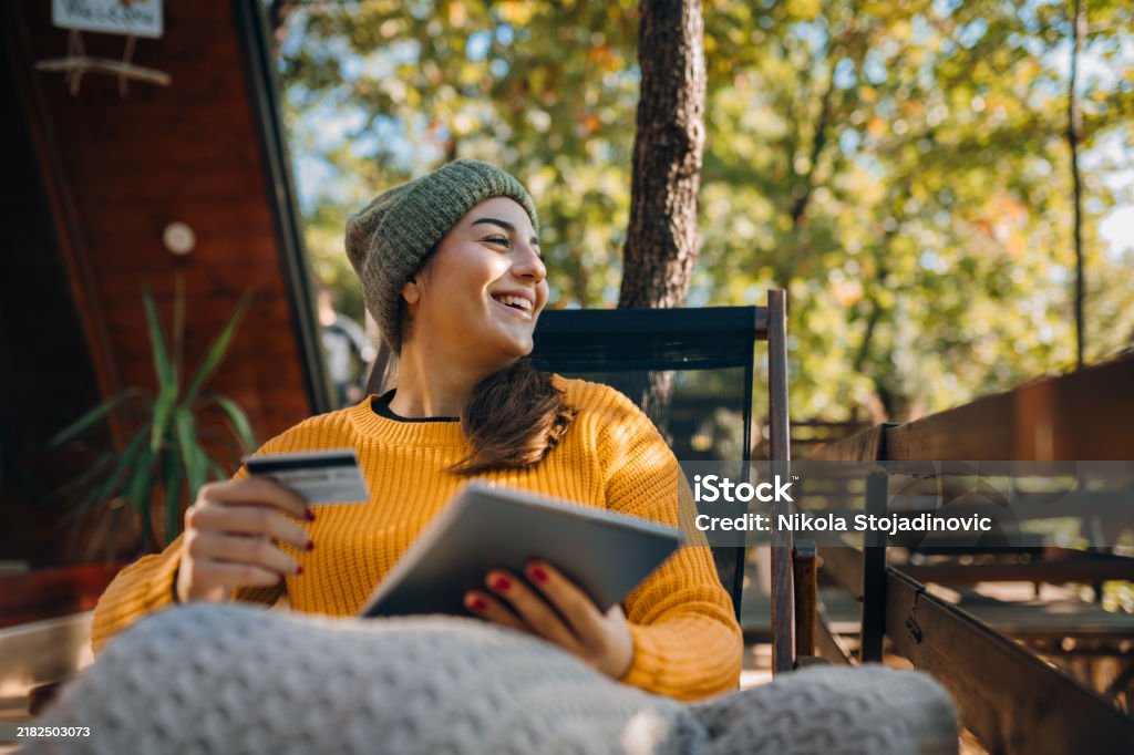 Young smiling brunette holding her debit card while using a digital tablet